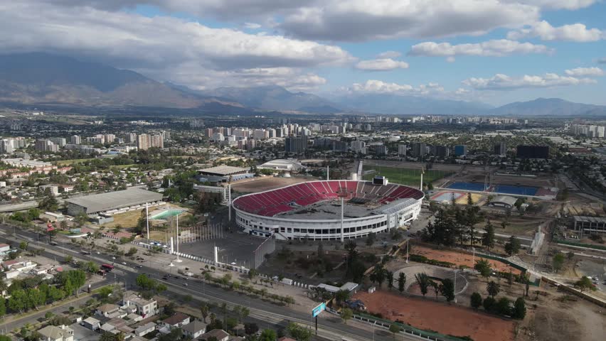 Aerial view of el teniente stadium in rancagua, chile, showcasing its urban setting with residential houses, mountains, and a cloudy sky