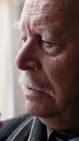 A contemplative elderly man is gazing thoughtfully out of a window, reflecting on life