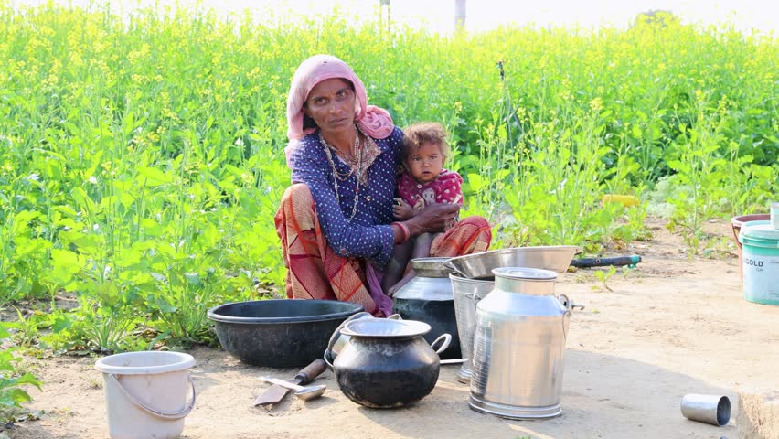 poor malnutrition village women living below poverty line holding baby with mustard fields behind