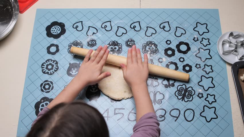 little Girl rolling dough on pastry mat with rolling pin, baking cookies