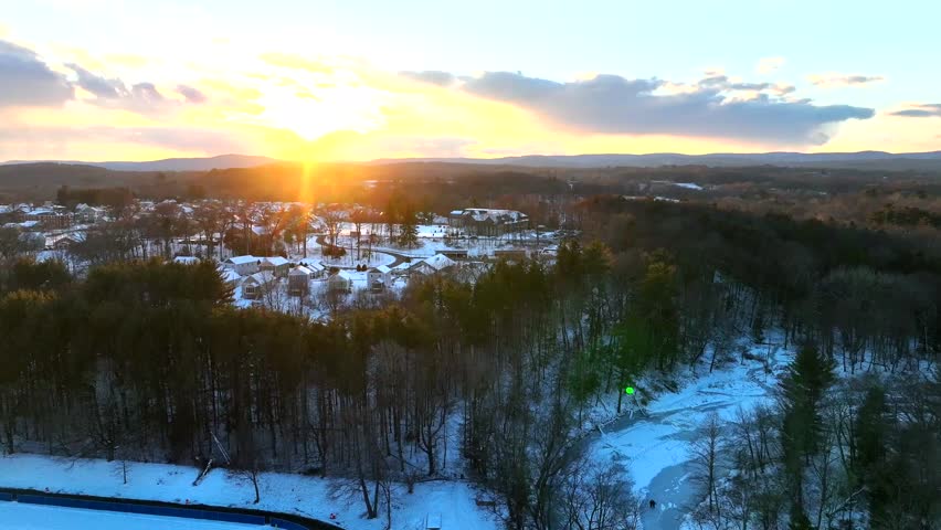 American suburb district with snowy houses and homes during golden sunset. Northampton Town, Massachusetts between leafless trees in Winter season. Aerial Wide shot.