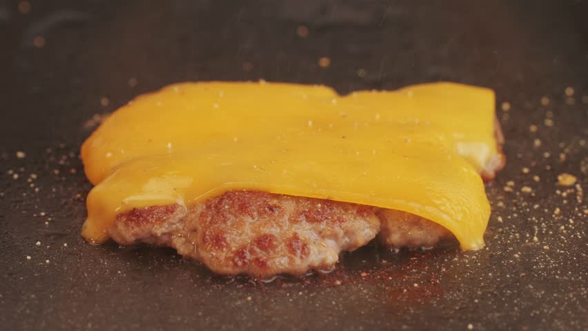 Cooking American fat smash burger with cheese slice on top on grill close-up. Beef or pork cutlet smashing by burger press. The chef in kitchen of the restaurant making cutlets for burgers - smash