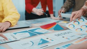 A diverse team collaborates on design concepts in a modern office, using color palettes and logo samples laid out on the table to inspire creativity and innovation. SACTR - Powered by Shutterstock - Get 15% off with code: PIKWIZARD15