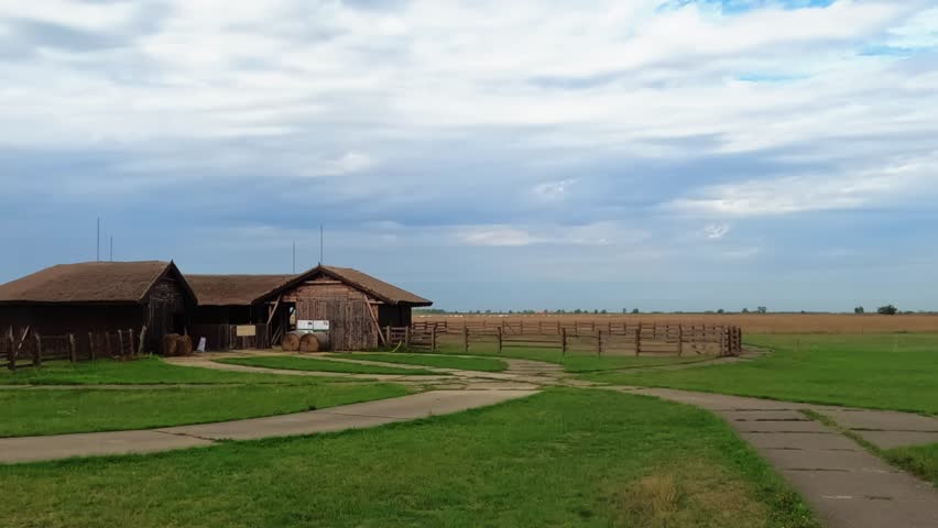 Idyllic timelapse from the Hortobagy National Park with an empty wooden barn and endless grassland on a cloudy day in Hungary.