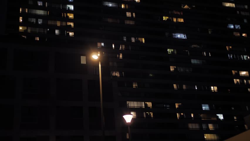 Moody urban shot from a moving car at night, capturing a towering apartment building with scattered glowing windows