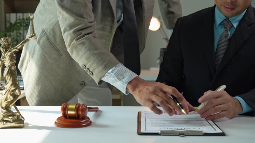 Professional businessmen completing legal contract signing at sleek white table, securing partnership through confident handshake with gavel representing formal business agreement
