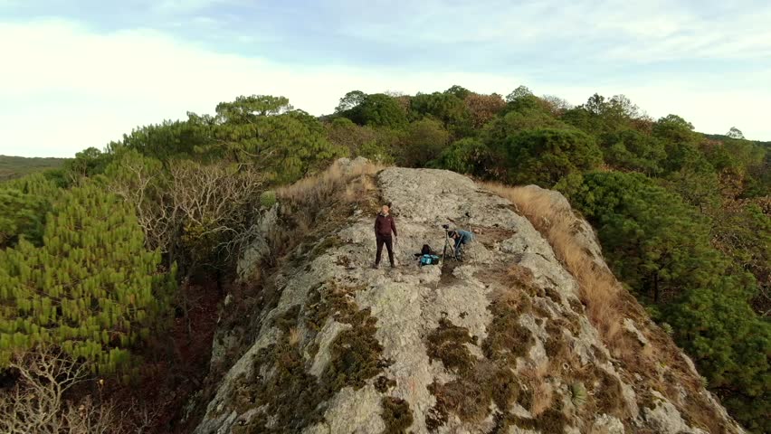 A drone view of two photographers climbed on a cliff surrounded by trees