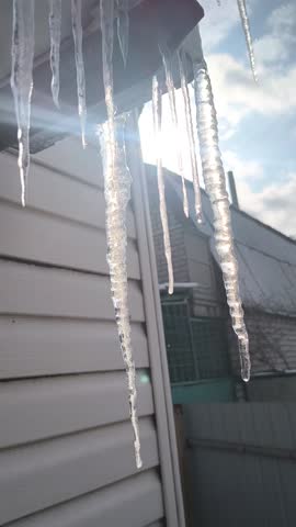 vertical video icicles on the roof. icicles melt in the sun.
