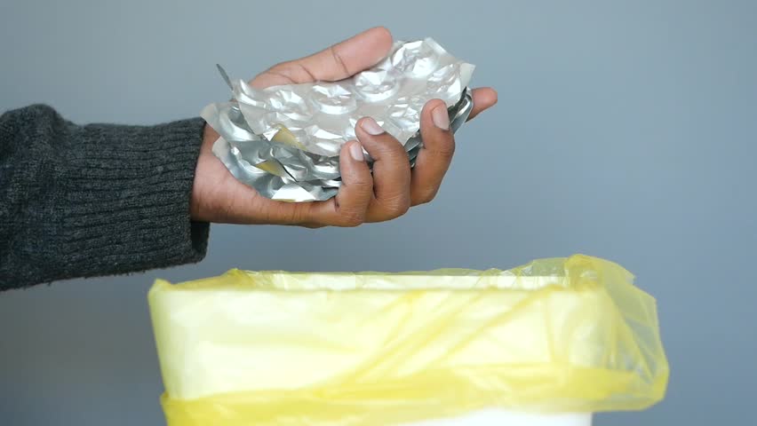 A hand is throwing away expired medicine packet into a trash can.