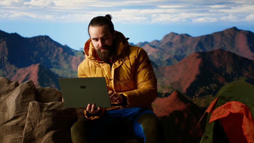 Nature lover workaholic always connected to the internet and scrolling on laptop, enjoying strong signal on a mountain top with a breathtaking landscape. Uninterrupted work. Camera B.