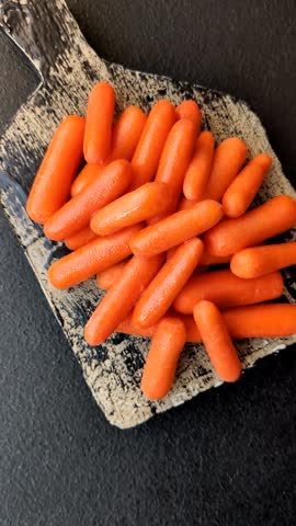 Raw peeled mini baby carrots as an ingredient for preparing a vegetarian food on a dark concrete background