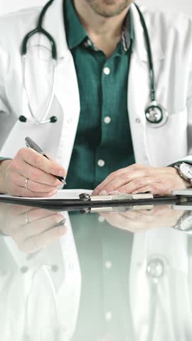 Male doctor using a clipboard and taking notes on glass desk in a medical office, close-up vertical view. Medicine concept