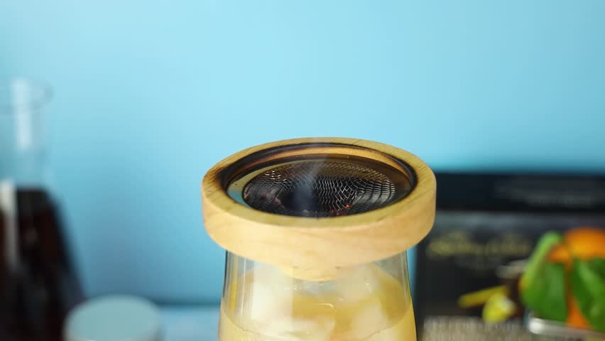Professional bartender wielding butane torch, igniting cocktail within glass container, creating dramatic fire effect during drink preparation at bar setting