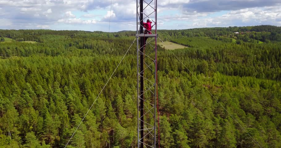 Telecommunications technician working at height climbing on a telecom tower, performing maintenance on 5G antenna.