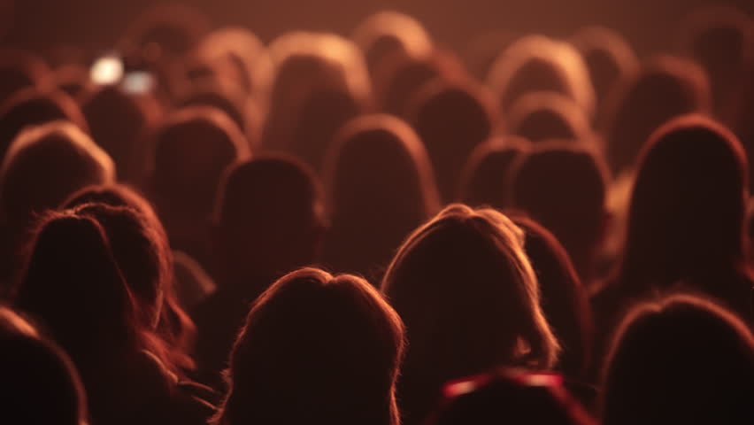 Many people in dark wait show start. Spectator ready watch epic film. Movie theater atmosphere. Fun teen audience before beginning. Joy cinema fans crowd sit at music concert hall. Orange night light.