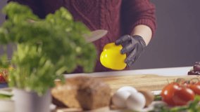 Slow-motion close-up of a chef slicing a yellow bell pepper on a wooden board. Black gloves ensure hygiene, while fresh ingredients like eggs, herbs, and bread create a vibrant kitchen setting - Powered by Shutterstock - Get 15% off with code: PIKWIZARD15