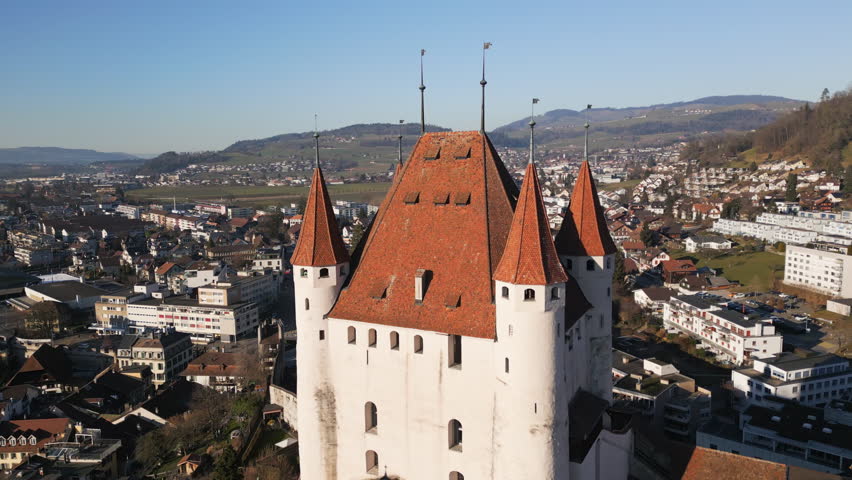 A stunning aerial view of a medieval castle in the historic old town of Thun, Switzerland, surrounded by charming rooftops, a scenic river, and majestic mountains