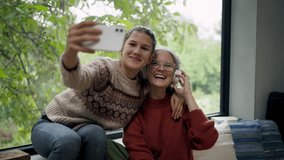 Mom and daughter sitting by big window, taking selfie. - Powered by Shutterstock - Get 15% off with code: PIKWIZARD15