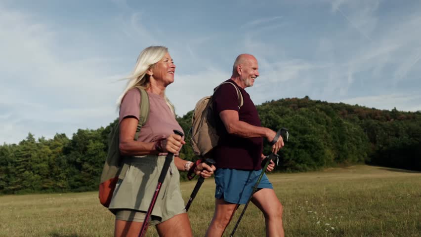 Active couple spending their free time outdoors, hiking in nature. Senior man and woman with trekking poles and backpack.