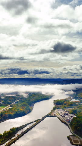 Aerial view of river valley with fog and sky reflection. Cumulus clouds. Autumn mountain landscape in the USA. Vertical video.