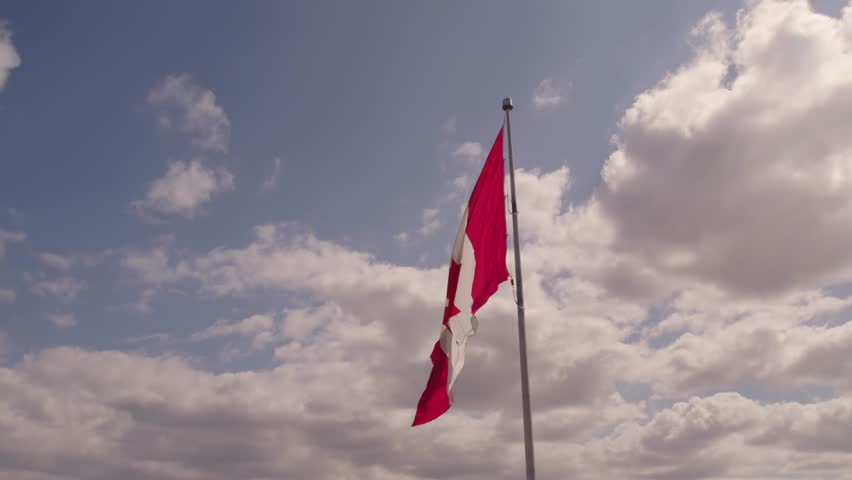 Flag of Canada flying against a summer blue sky. Canadian flag waving on the wind. Canadian flag with maple leaf on the pole slow motion movement.