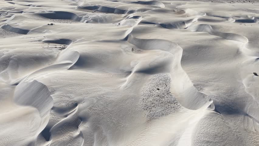 Sweeping sand dunes create a surreal landscape in White Sands, New Mexico, with intricate wind-sculpted ridges and isolated patches of rock contrasting against the pristine gypsum.