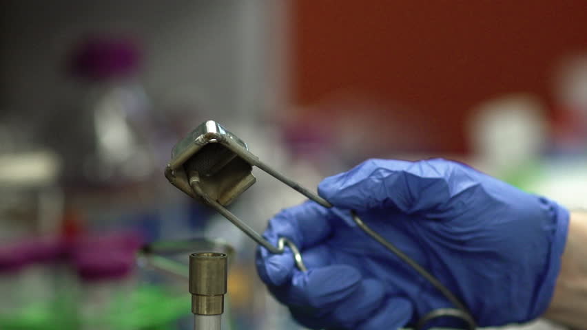 A lab technician uses a lighter to ignite a Bunsen burner.