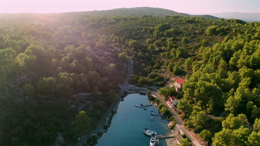 Backward panoramic flight over serene bay with sailboats and yachts at sunset on Solta Island, Croatia.