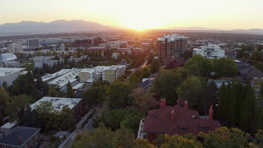 Aerial drone shot of the west Salt Lake Valley from Capital Hill, dollying in over homes, apartments, and small roads. Vibrant fall trees glow in the golden-orange hues of a colorful autumn sunset.