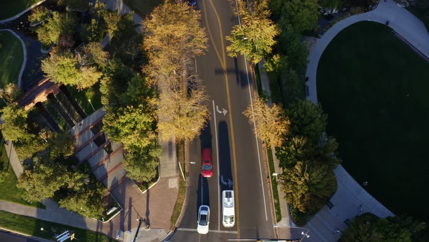 Aerial drone shot of a small street in downtown Salt Lake City. The camera flys forward from a bird’s-eye view over passing cars, surrounded by fall trees glowing in the golden hues of autumn.