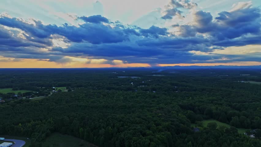 A drone fly-over of Greenville County in South Carolina showing a landscape of trees, mountains, and storm clouds.