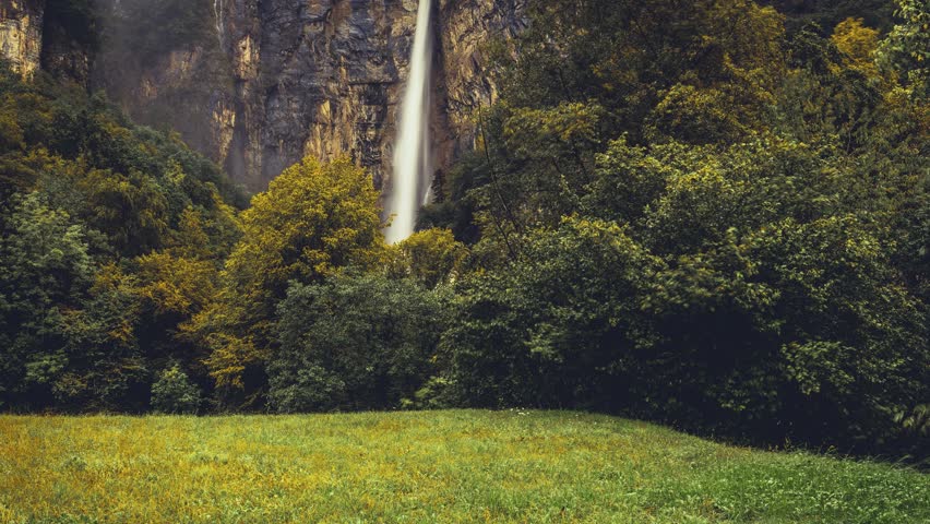 Two towering waterfalls cascade down rugged cliffs, framed by vibrant autumn foliage in Amden, St. Gallen, Switzerland. Misty air adds a dreamy, cinematic feel. (moving Timelapse)