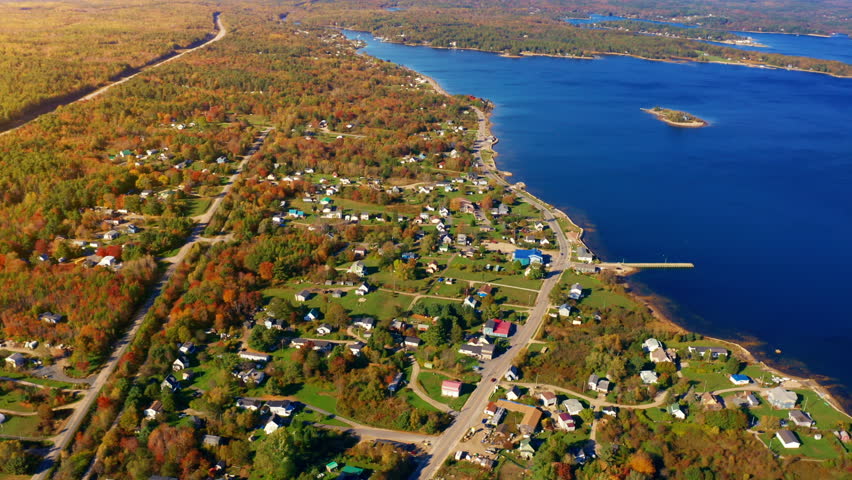 Aerial drone shot over the coastline of Oak Island, Nova Scotia, Canada.
High view of the sea, autumn colorful trees foliage. Picturesque landscape. Fall vibrant colors.