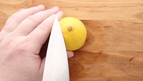 A hand holds a fresh lemon while a knife makes an incision on a wooden cutting board. The bright yellow citrus fruit is ready for squeezing, cooking, or garnish. - Powered by Shutterstock - Get 15% off with code: PIKWIZARD15