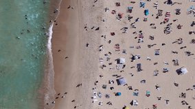 Downward angle aerial shot of Bondi Beach, highlighting sunbathers, swimmers, and surfers along the famous Australian coast. Rising aerial footage. - Powered by Shutterstock - Get 15% off with code: PIKWIZARD15