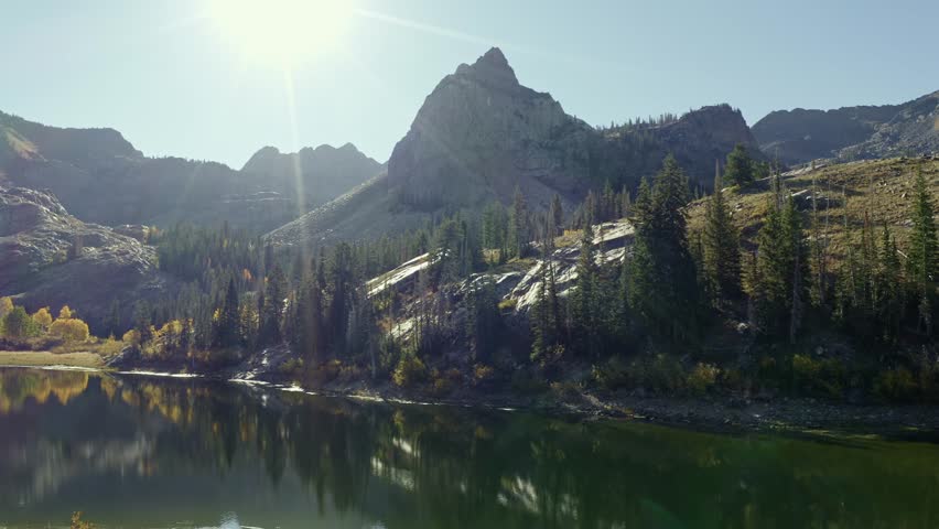 Aerial drone shot of Lake Blanche in Utah’s Big Cottonwood Canyon. The camera tilts up and dollys in, revealing golden aspens, green pines, and the alpine lake framed by a towering mountain in autumn.