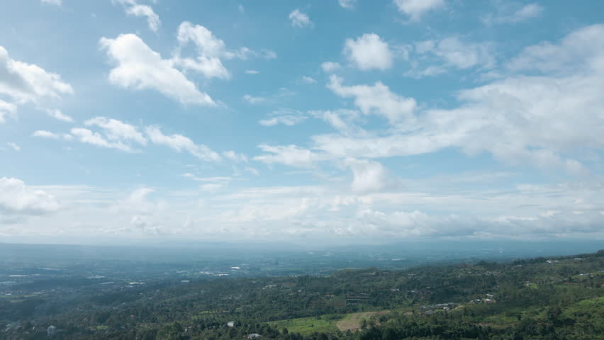 A cinematic aerial drone view of lush green hills meeting a bright blue sky with soft, scattered clouds. This footage is ideal for background visuals, travel content, and relaxation themes