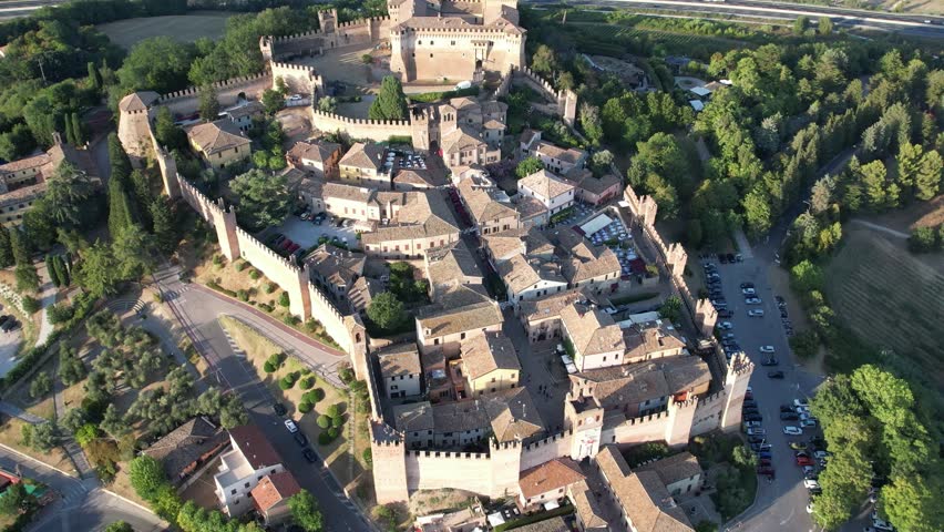 Aerial shot capturing the fortified Gradara Castle in Marche, Italy, showcasing the medieval walls, traditional buildings, and greenery. The castle’s strategic hilltop location is clearly visible