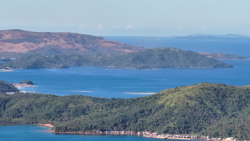 Coastline with houses in tropical island surrounded by blue sea. Mindanao, Philippines. Zoom view.