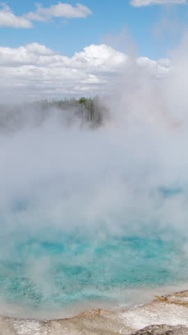 A stunning and beautiful hot spring located within Yellowstone National Park, presenting vibrant blue water that is beautifully surrounded by steam and complemented by a picturesque sky overhead