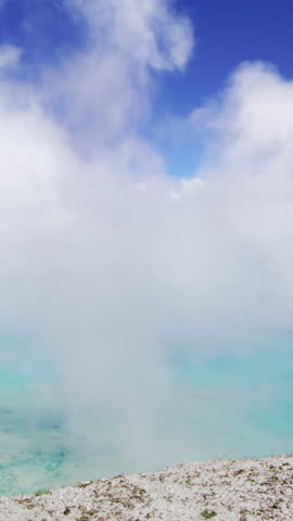 A misty and serene scene beautifully showcasing the stunning thermal waters of Yellowstone National Park in Wyoming, elegantly surrounded by soft clouds and bright blue skies above
