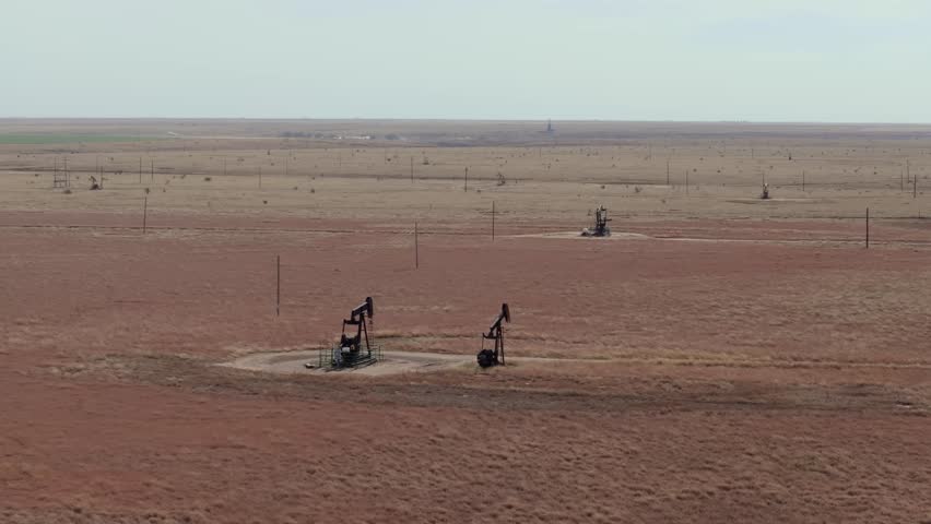 Oil pumps in a vast, dry texas landscape, showing industrial activity, aerial view