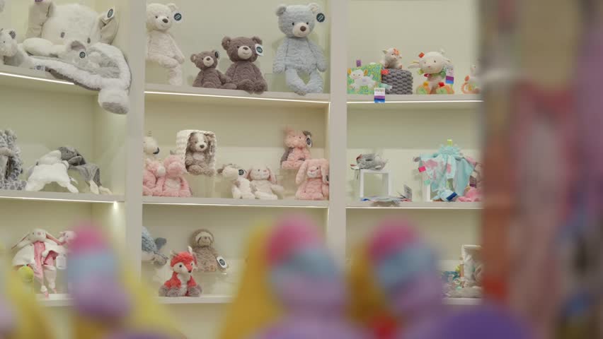 Various plush toys, teddy bears, and baby accessories arranged on illuminated shelves at a toy fair. A cozy and charming display of stuffed animals and infant gifts.
