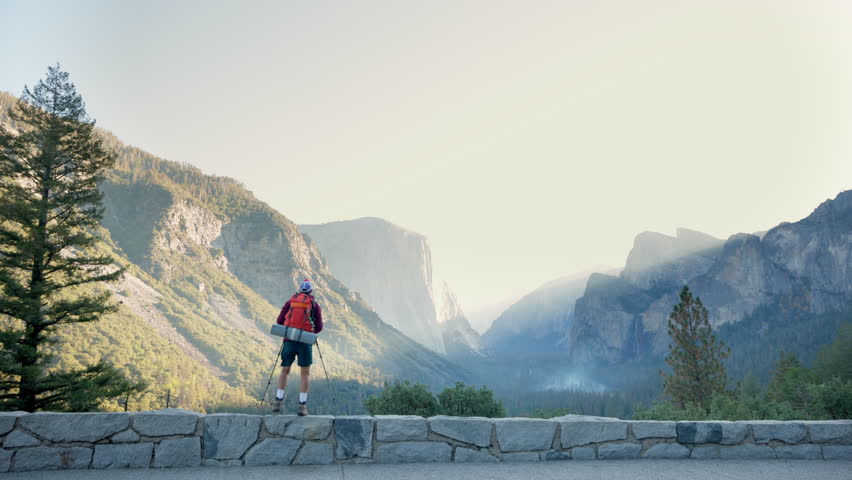 Hiker revels in the breathtaking scenery offered by Yosemite National Park, showcasing iconic landmarks such as El Capitan and Half Dome, all framed by the exquisite beauty and charm of nature