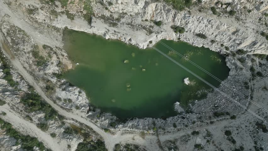 Green water gradually filling quarry basin during descending camera movement, revealing submerged rocks and dense algae beneath water surface