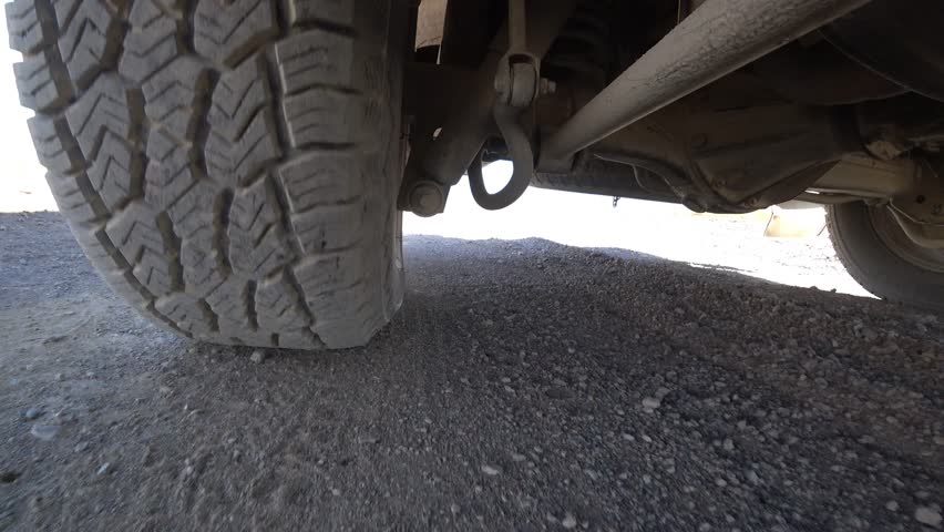 The camera is fixed on the bottom of the car, a view of the wheel and suspension while driving. Off-road, rocks and dust. The suspension works well off-road and bumps. Deserted area. Tire deformation