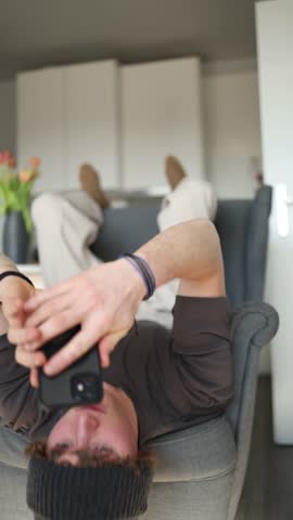 Vertical screen: A student is laying on a chair, scrolling through their phone. Their posture shows how modern technology has become a constant companion, even in moments of relaxation.