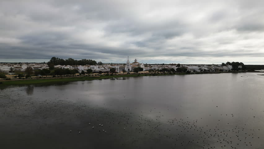 El Rocio town with white buildings near calm lake on moody day, aerial view