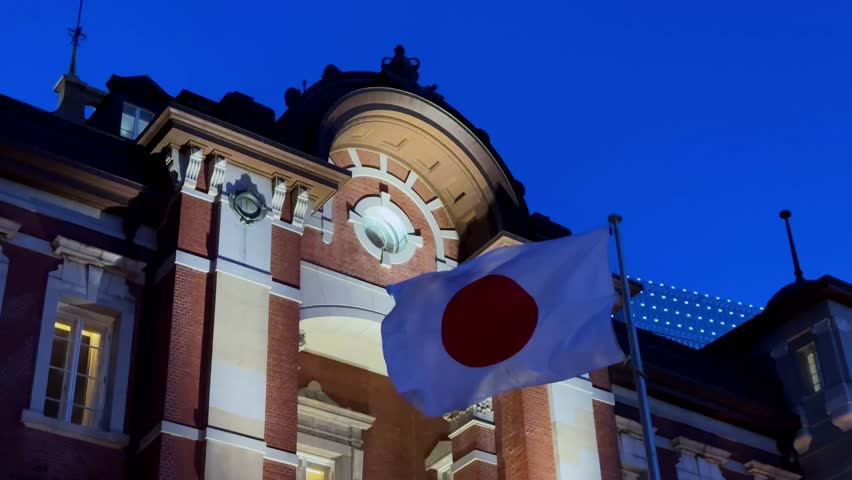 Tokyo Station at night with a Japanese flag waving against a deep blue sky