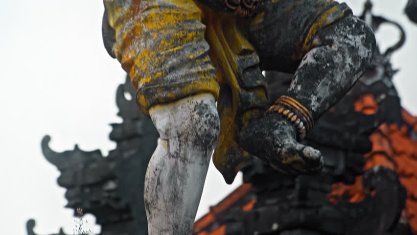 An old stone statue of Ganesha covered with moss, standing on the street 